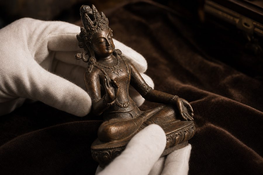 White-gloved hands inspecting a small antique bronze sculpture on velvet
